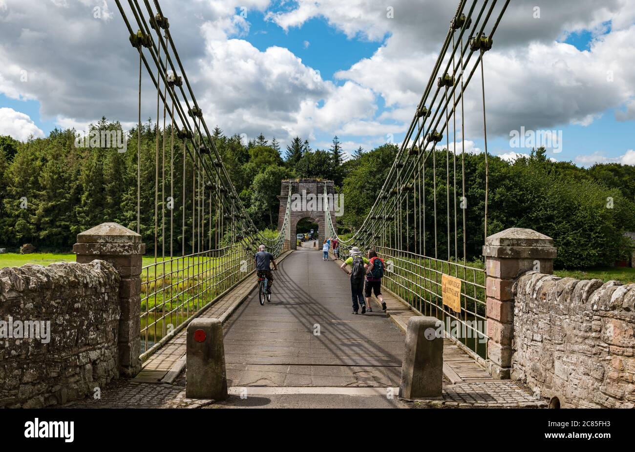 River Tweed, Englisch/Schottische Grenze, Großbritannien, 21. Juli 2020. 200 Jahre Union Bridge: Die Brücke feiert am 26. Juli ihr 200-jähriges Bestehen. Es war die erste Fahrzeugaufhängung Brücke in Großbritannien. Zur Zeit ihrer Errichtung war sie mit 137 m die längste schmiedeeiserne Hängebrücke der Welt. Es wird immer noch regelmäßig von Fußgängern, Radfahrern und Autos verwendet, aber Autos müssen es zu einer Zeit überqueren. Diese Ansicht ist von der englischen Grenze. Die Leute gehen über die Brücke Stockfoto