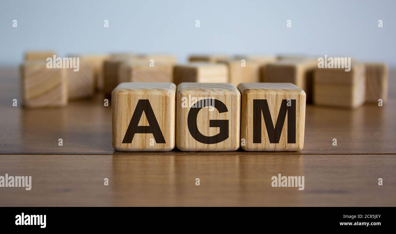 Konzept Wort "AGM" - Akronym von Worten "Jahreshauptversammlung" auf Würfel auf einem schönen Holztisch. Weißer Hintergrund. Geschäftskonzept. Stockfoto