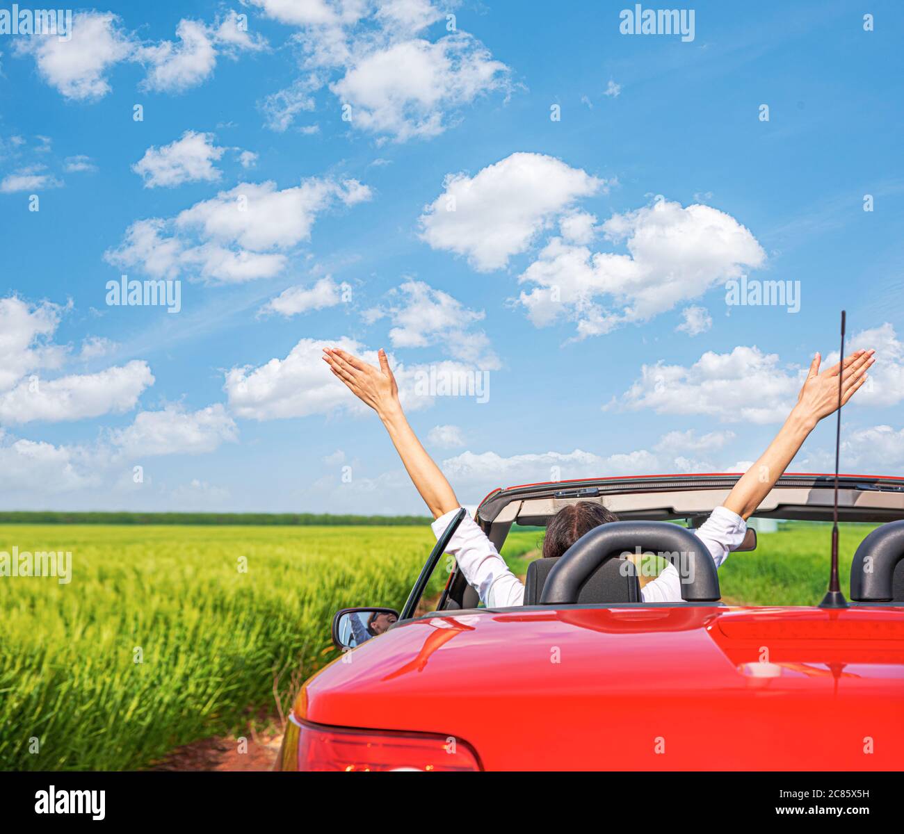 Frau in einem roten Auto vor dem Hintergrund eines Feldes außerhalb der Stadt. Stockfoto