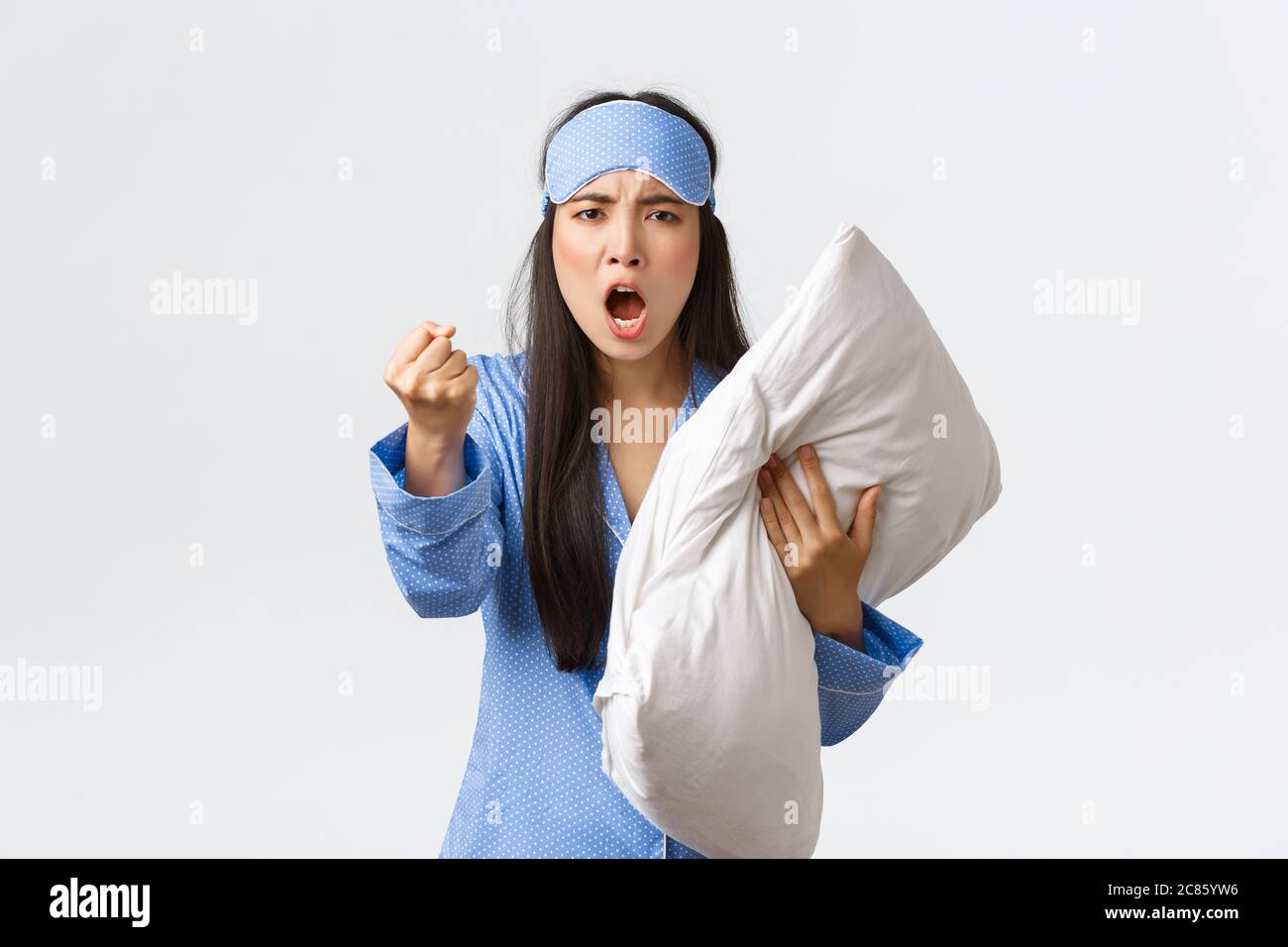 Wütend und belästigt erschöpft asiatische Mädchen beschweren laute Nachbarn im Schlafsaal, tragen Schlafmaske und Pyjama, halten Kissen und bedrohen jemanden Stockfoto