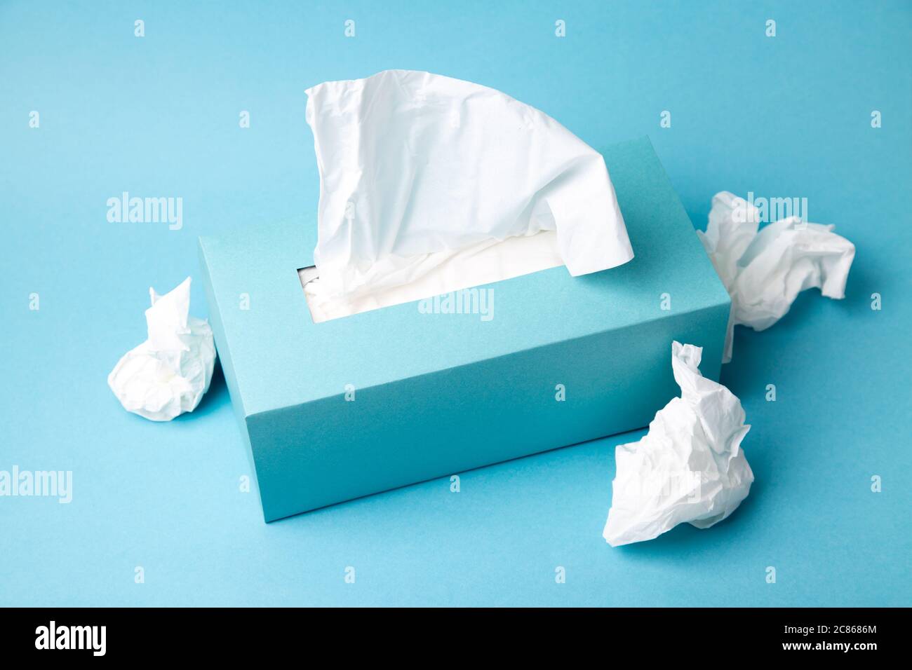 Hellblaue Gewebebox und zerknitterte Gewebe auf blauem Hintergrund. Erkältungs- und Grippekonzept. Minimale monochromatische Zusammensetzung. Stockfoto