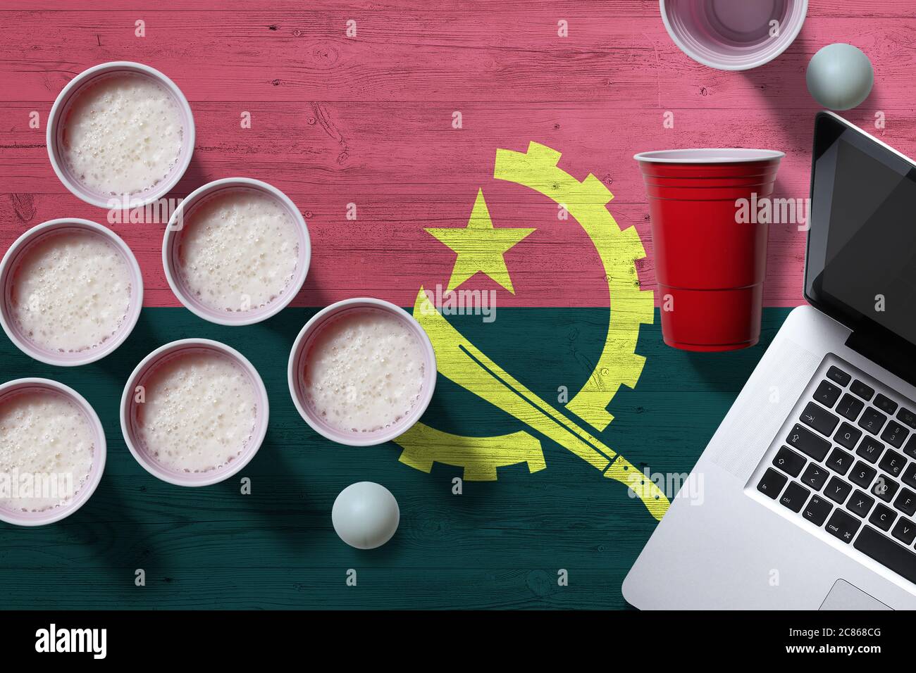 Angola-Flagge-Konzept mit Kunststoff-Bier-Pong-Tassen und Laptop auf nationalen Holztisch, Draufsicht. Bier Pong Spiel. Stockfoto