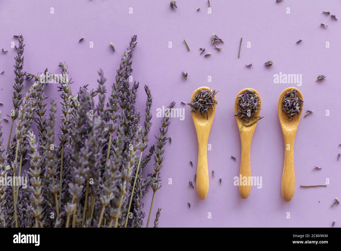 Trockene Lavendelblüte in Holzlöffel und Lavendelbukett auf violettem Hintergrund Stockfoto