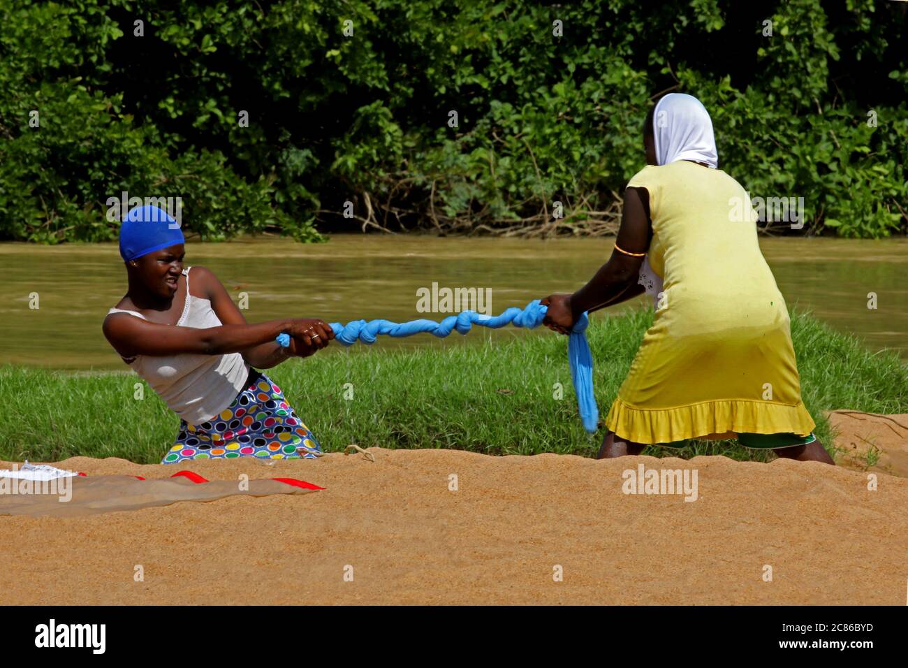 Die Kleidung in Ghana auswringen. Zwei Frauen wringen ein Tuch, das gerade an einem Flussufer gewaschen wurde. Stockfoto