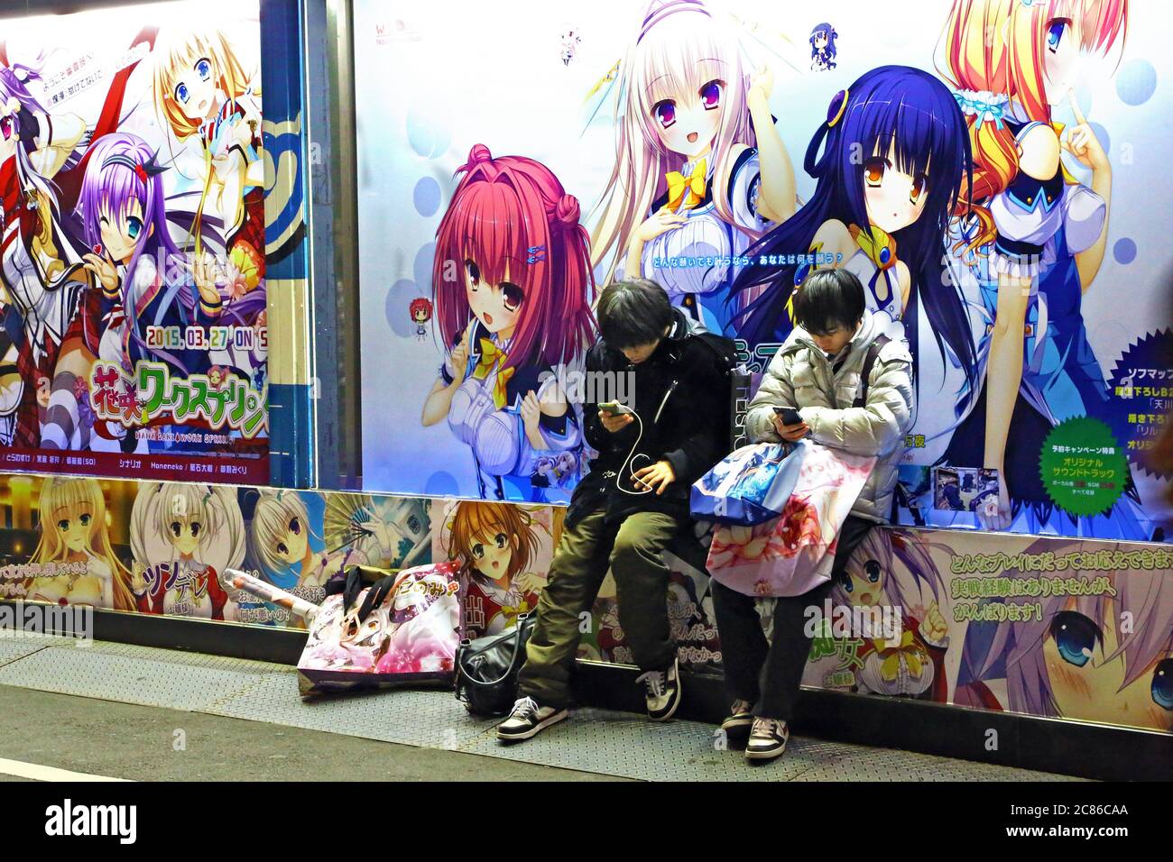 Jugendliche im Asakusa-Viertel, Tokio. Zwei Teenager nutzen ihre tragbaren Geräte. An der Wand dahinter Zeichnungen von Manga. Stockfoto