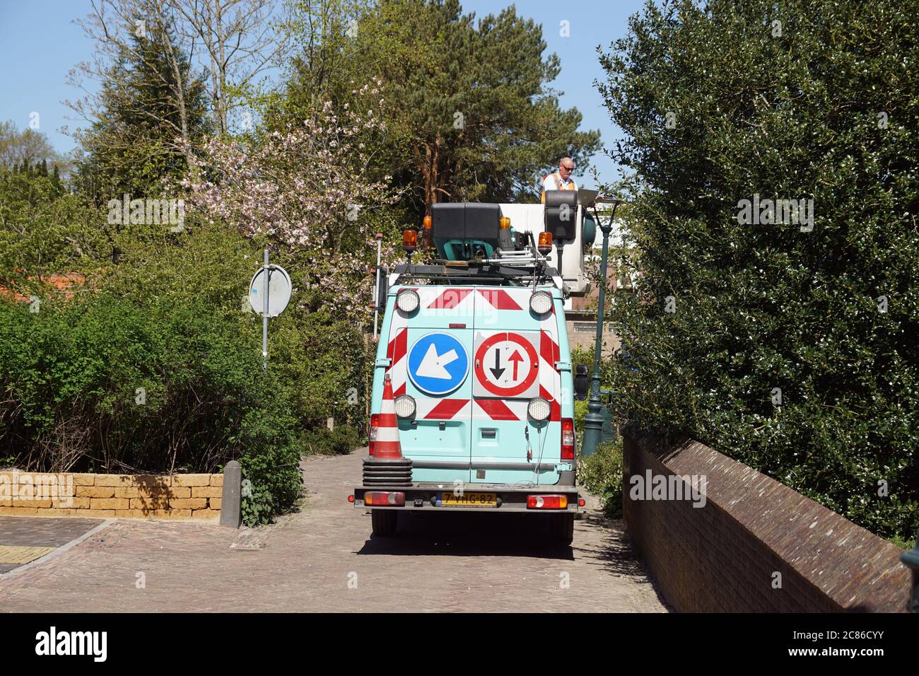 Ein Mann in einem Eimer eines Teleskopauslegers auf einem LKW repariert die Straßenlampe. Straßenschilder hinter dem Auto. Bergen. Niederlande, April Stockfoto