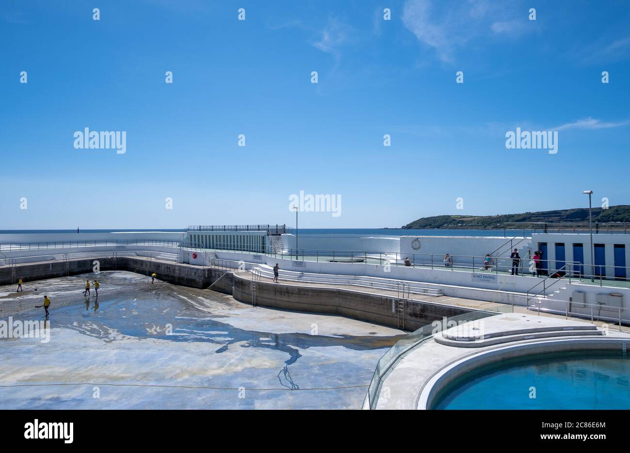 Rettungsschwimmer reinigen Algen auf dem Boden des Jubilee Pool, Penzance; vor der Wiederfüllung und Wiedereröffnung am 25. Juli 2020 nach dem Coronavirus Lockdown. Stockfoto