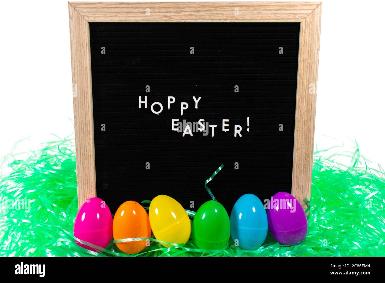 Ein schwarzes Schild mit einem Birkenrahmen, der Frohe Ostern in weißen Buchstaben mit einem Satz Regenbogen Eier und grünes Ostergras vor ihm auf einem reinen Whi sagt Stockfoto
