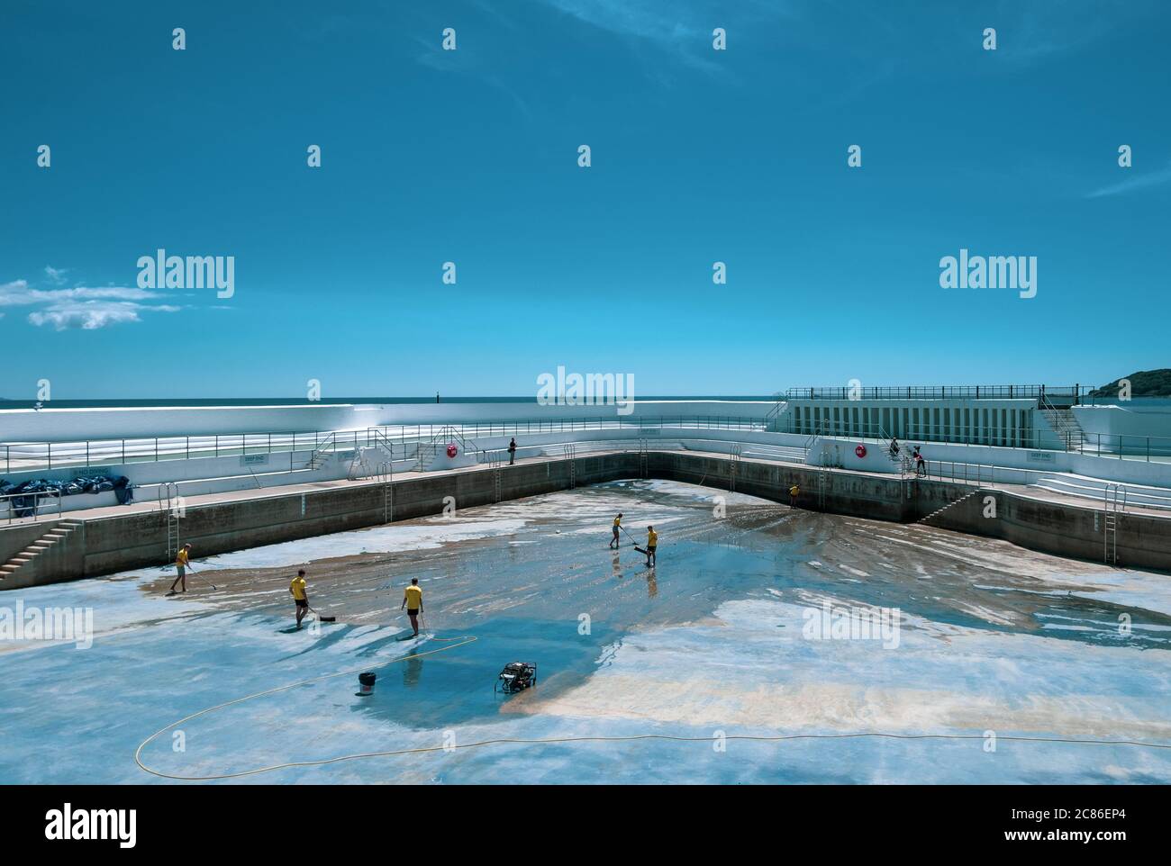Rettungsschwimmer reinigen Algen auf dem Boden des Jubilee Pool, Penzance; vor der Wiederfüllung und Wiedereröffnung am 25. Juli 2020 nach dem Coronavirus Lockdown. Stockfoto