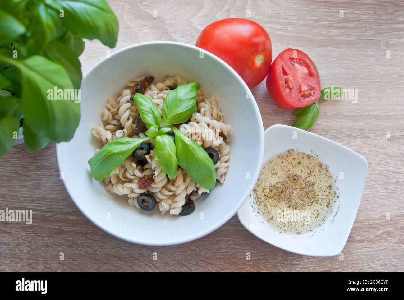 Leckere Pasta mit Oliven, getrockneten Tomaten und Kräuterdressing. Dekoriert mit Basilikum und frischen Tomaten auf Holzhintergrund. Diät-Mahlzeit. Stockfoto