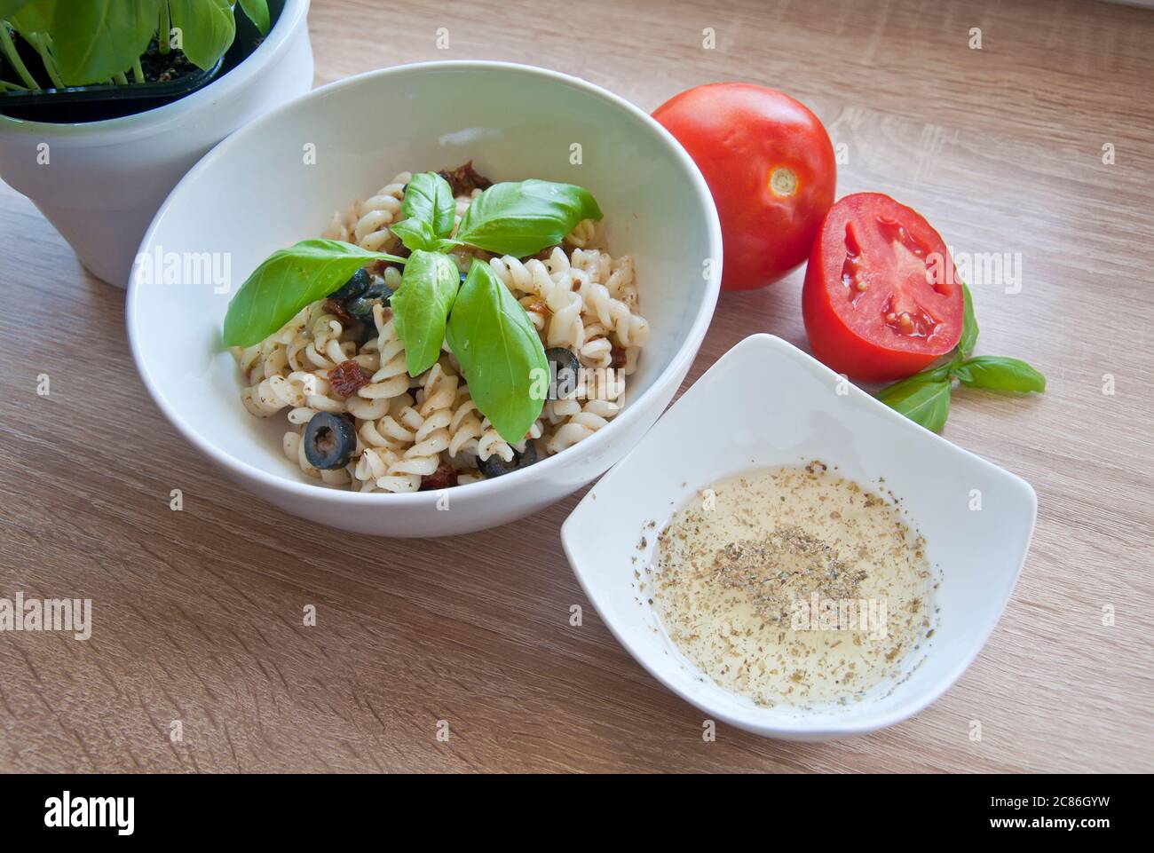 Leckere Pasta mit Oliven, getrockneten Tomaten und Kräuterdressing. Dekoriert mit Basilikum und frischen Tomaten auf Holzhintergrund. Diät-Mahlzeit. Stockfoto