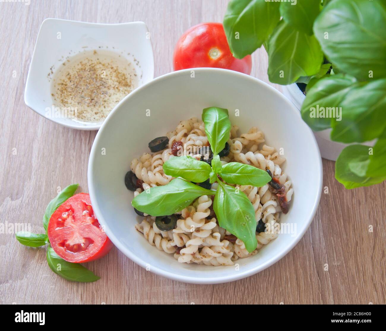 Leckere Pasta mit Oliven, getrockneten Tomaten und Kräuterdressing. Dekoriert mit Basilikum und frischen Tomaten auf Holzhintergrund. Diät-Mahlzeit. Stockfoto