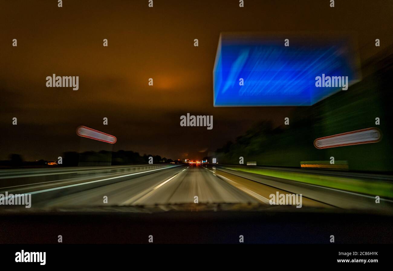 Die Langzeitaufnahme einer Autobahn in der Nacht während der Fahrt über eine deutsche Autobahn und ein typisches blaues Schild. Stockfoto