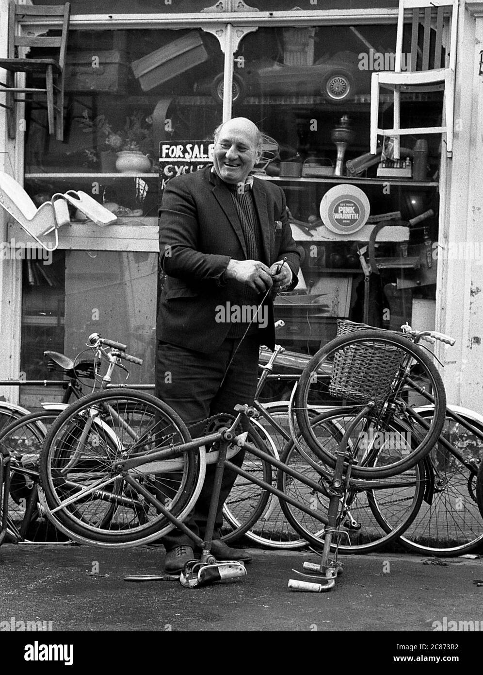 AJAXNETPHOTO. JANUAR 1975. SOUTHSEA, PORTSMOUTH, ENGLAND. - FAHRRADREPARATUREN - DER BESITZER DES SKIPPERS FAHRRADLADENS VOR DEM GELÄNDE MIT SEINEM HUND AN DER ECKE FONTWELL UND MARMION ROAD. FOTO: JONATHAN EASTLAND/AJAX REF:7504 202206 27 Stockfoto