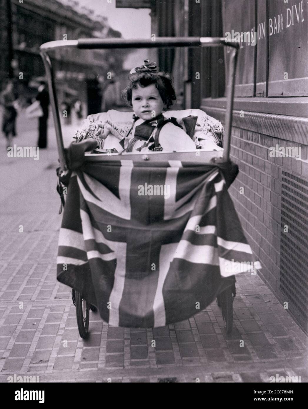 VE-Tag. Ein Baby sitzt stolz in einem Kinderwagen, der am VE-Tag mit einer Union-Jack-Flagge bestückt ist. Stockfoto