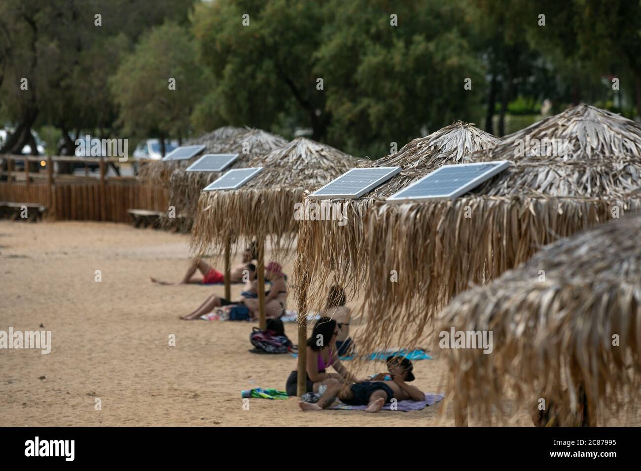 (200721) -- ATHEN, 21. Juli 2020 (Xinhua) -- das Foto vom 21. Juli 2020 zeigt Sonnenkollektoren auf Sonnenschirmen an einem öffentlichen Strand in der Nähe des Rathauses der Gemeinde Vari-Voula-Vouliagmeni im Süden Athens, Griechenland. Ab Dienstag sind die Dutzende von Sonnenschirmen, die entlang des Strandes verteilt sind, gemäß den sicheren Entfernungsmaßnahmen zum Schutz gegen COVID-19, mit einem System aus Solarmodulen und USB-Anschlüssen ausgestattet, das kostenlos und umweltfreundlich aufgeladen werden kann. Im Rahmen eines am Dienstag gestarteten Pilotprogramms werden Sonnenanbeter mit Hilfe von Solar e zu Energieeinsparungen beitragen Stockfoto