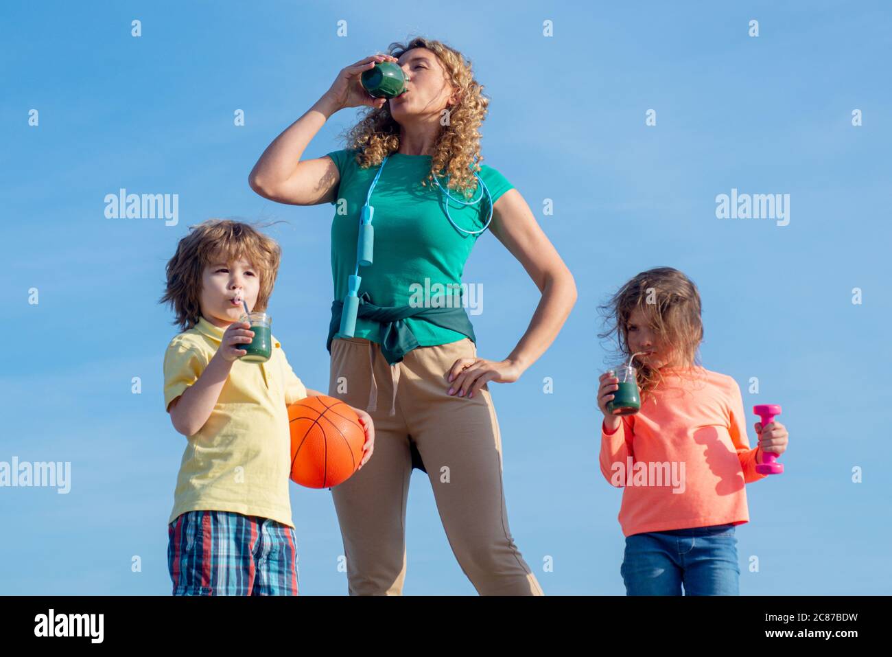 Mama und Kinder trinken Smoothie oder Saft. Familie nach Sport Training auf blauem Himmel Hintergrund, kopieren Raum. Glücklich lachende Kinder und sie Stockfoto