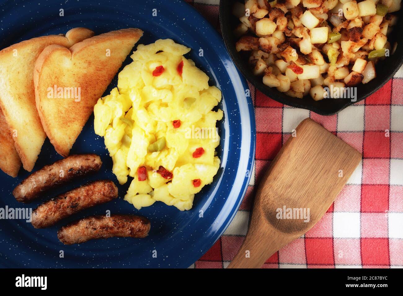 Rustikales Rühreier-Frühstück mit Paprika, Wurst und Toast auf einem rustikalen Holztisch mit warmen Licht. Stockfoto