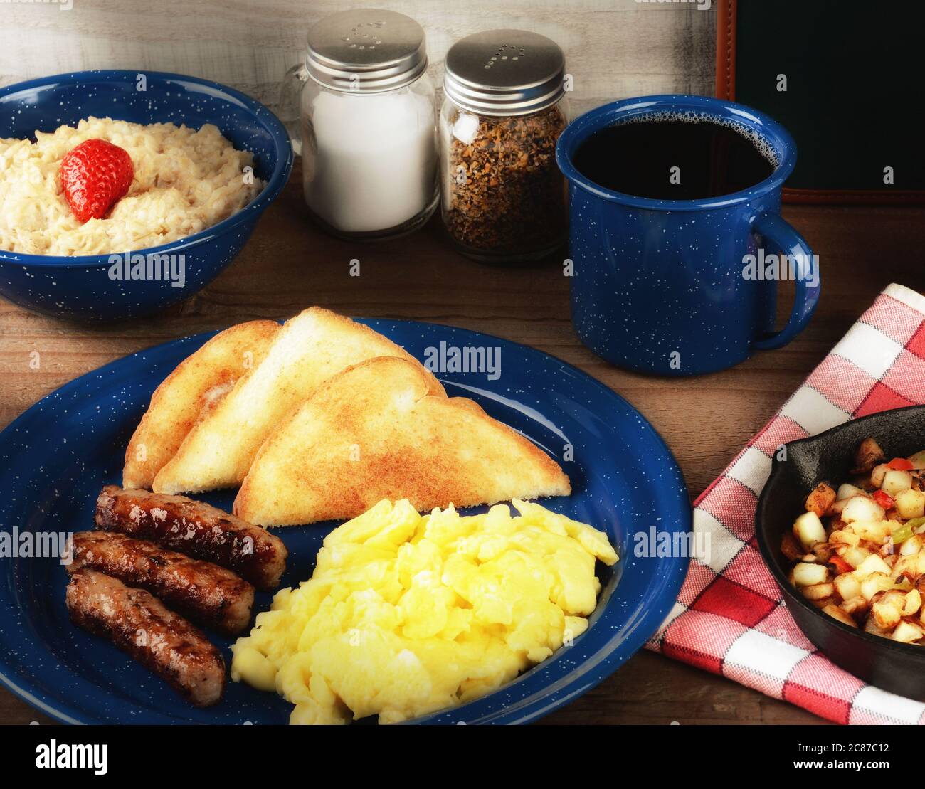 Ein rustikales Rührei-Frühstück auf einem rustikalen Holztisch mit Haferbrei, Kartoffeln und Kaffee mit warmer Beilage. Stockfoto