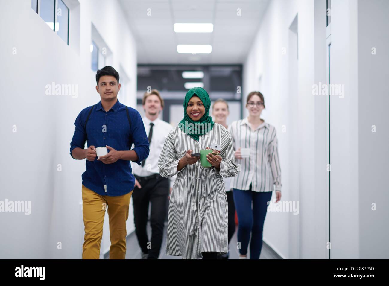 Multiethnisches Startup-Business-Team, das durch den Flur des Gebäudes geht, während es von einer Kaffeepause zurückkommt Stockfoto
