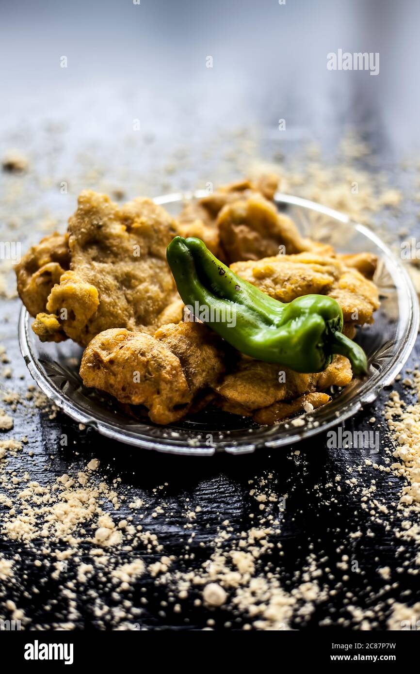 Berühmte Aloo pakora/ aloo bhajia in einer Glasplatte mit grünem Chili und etwas Kichererbsenmehl auf einer Oberfläche verteilt.Schuss von alu bhajiya auf einem transparenten gla Stockfoto