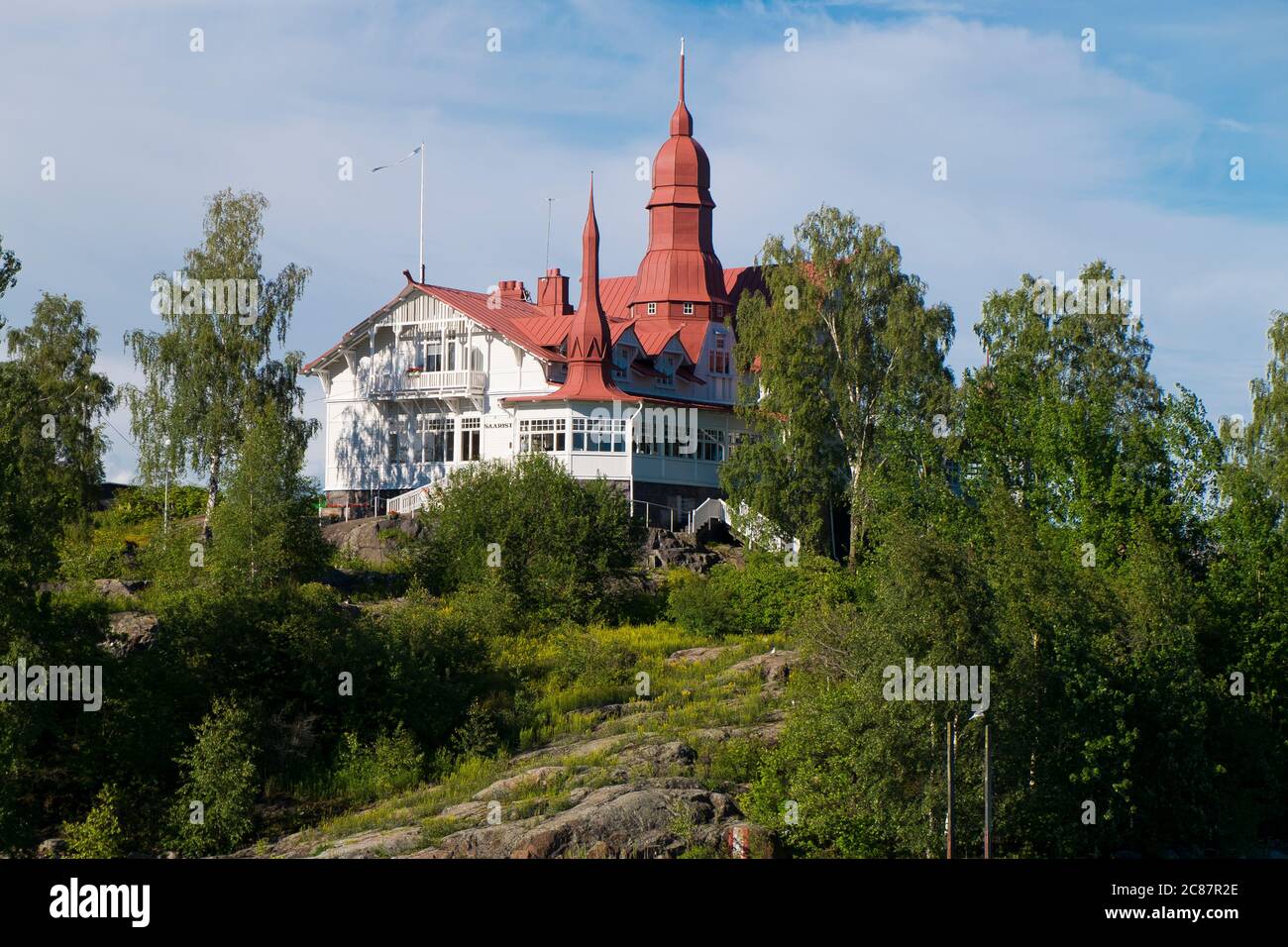 Auf einer Anhöhe auf einer der vielen Inseln thront ein altes, ikonisches, weißes viktorianisches Herrenhaus mit einem Metalldach. Kreuzfahrt auf dem Finnischen Meerbusen in der Nähe von Helsinki. Stockfoto