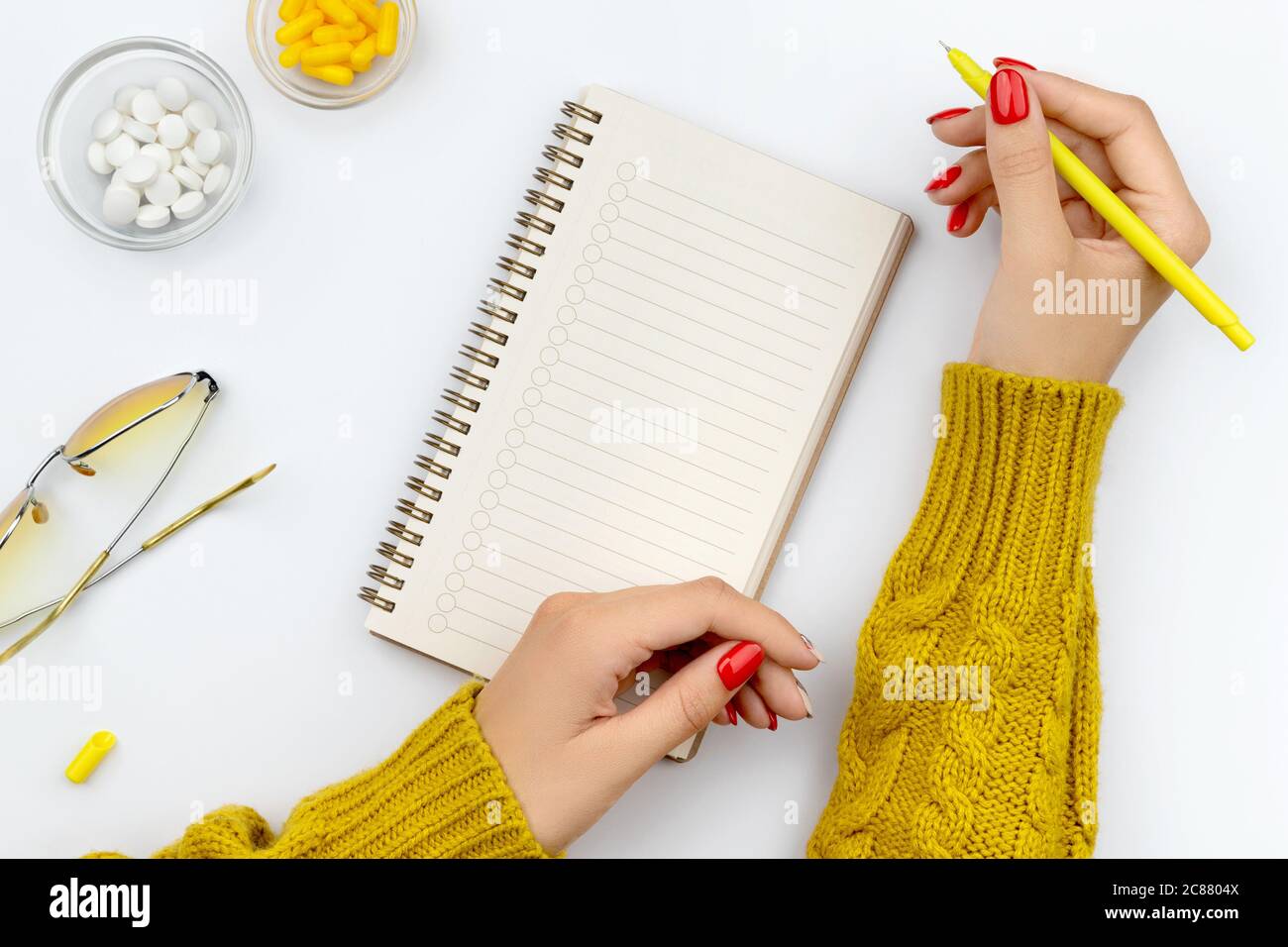 Weibliche gepflegte Hände schreibt in einem Notizblock mit Pillen auf dem Hintergrund. Konzept der Gesundheitsfürsorge Stockfoto