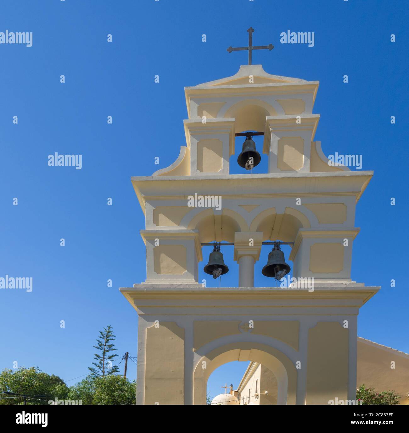 Traditioneller griechischer freistehender Glockenturm an der Kirche in Sidari, gelber weißer Glockenturm mit drei Glocken und Kreuz bei Sidari, Korfu Griechenland, blauer Himmel Stockfoto