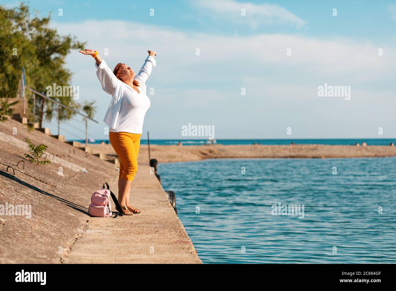 Die übergewichtige Frau hob ihre Hände vor Freude. Meer auf dem Hintergrund. Speicherplatz kopieren. Seitenansicht. Stockfoto