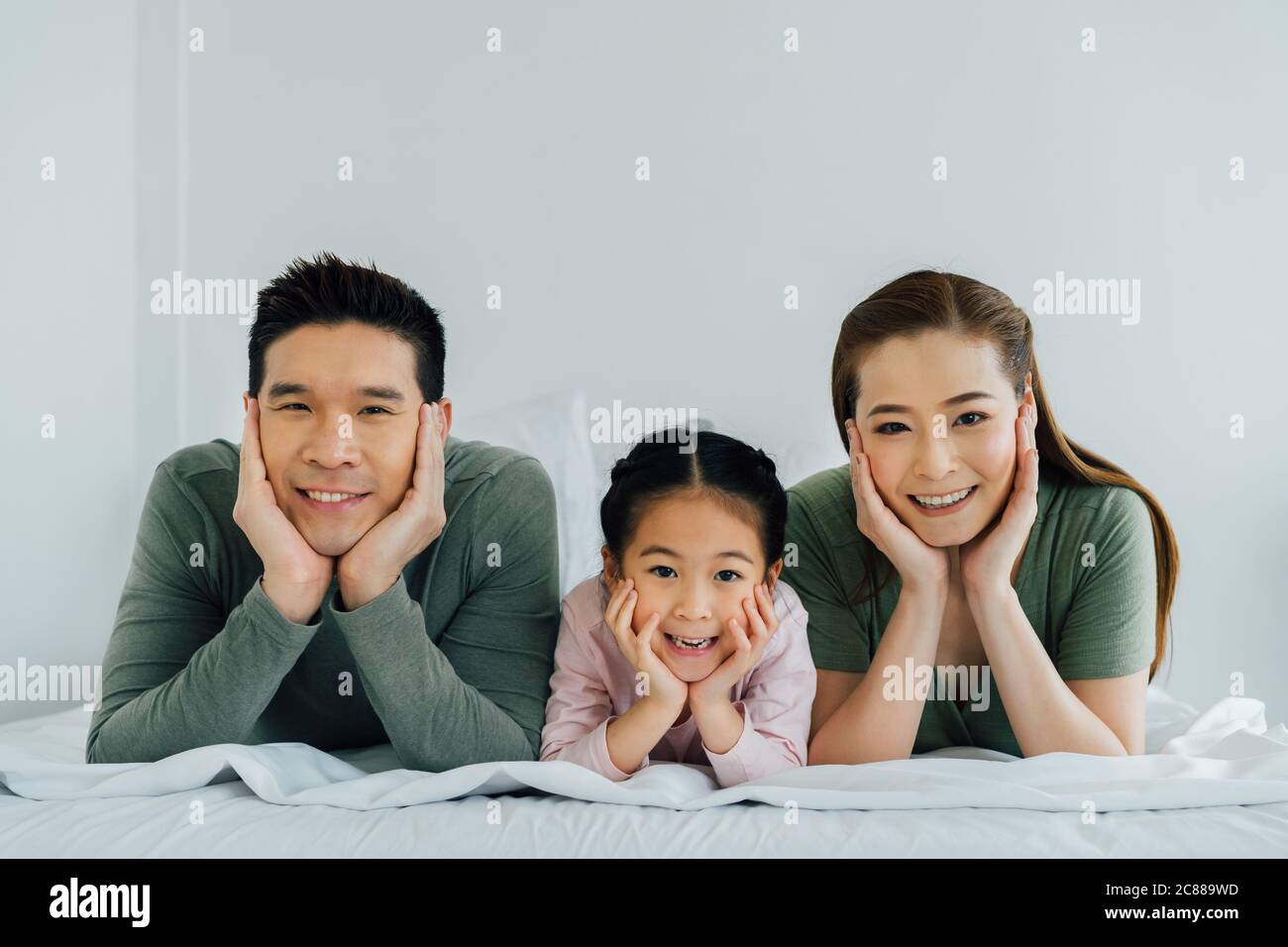 Chinesische Mutter und Vater mit jungen Tochter, die sich an Ellbogen lehnt und lächelt Stockfoto