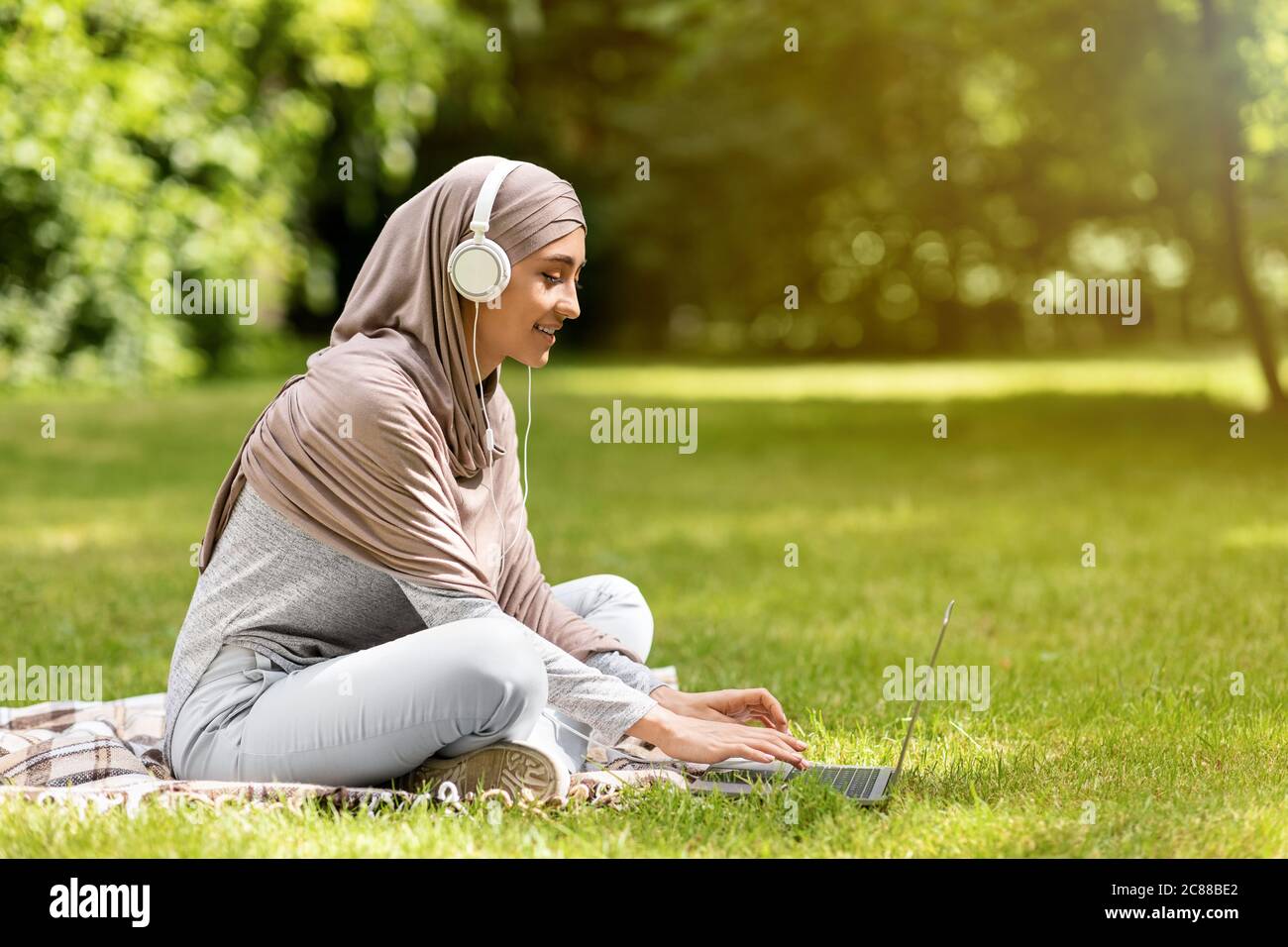 Muslimische Mädchen beim Film auf Laptop im Park Stockfoto