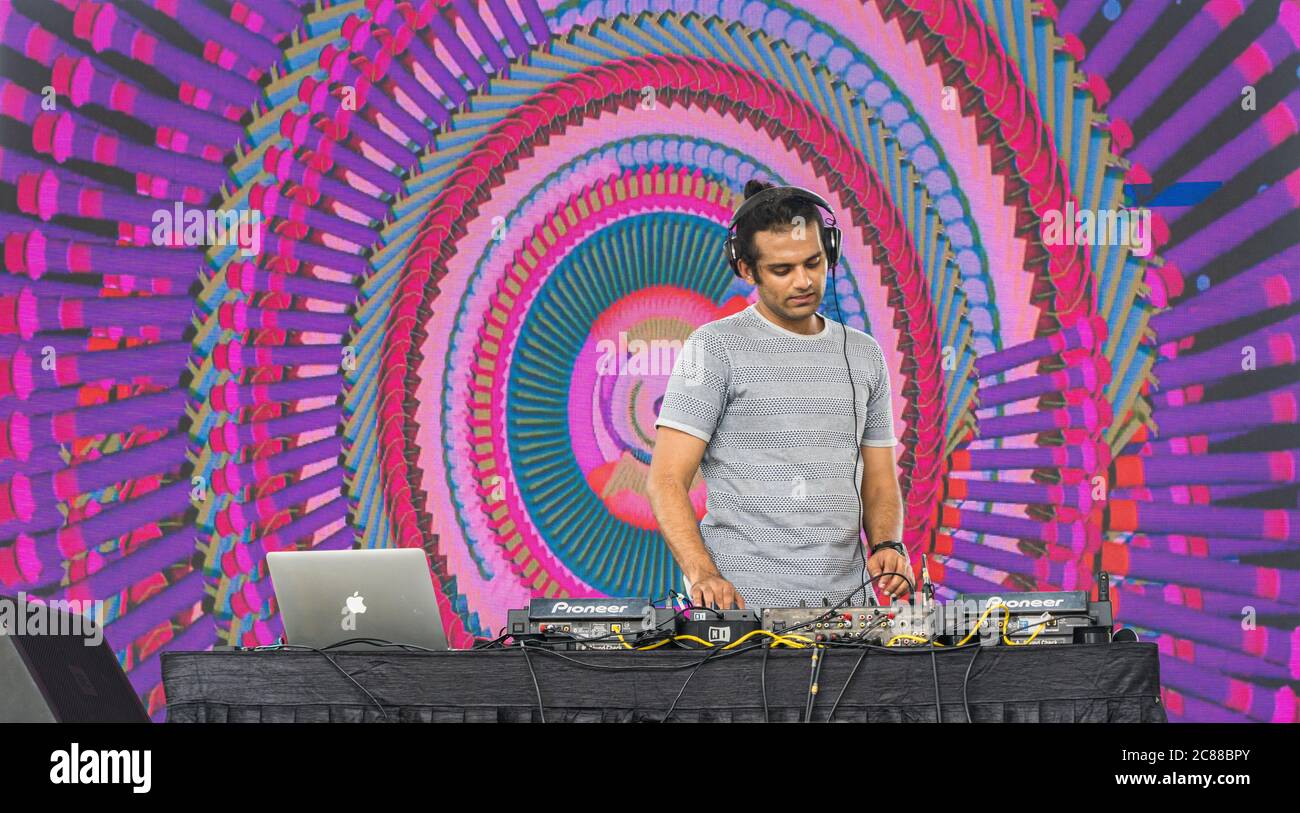 Ein professioneller DJ, der bei einem Festival Musik spielt, mit digitalen DJ-Plattenspielern und abstrakten Visuals im Hintergrund Stockfoto