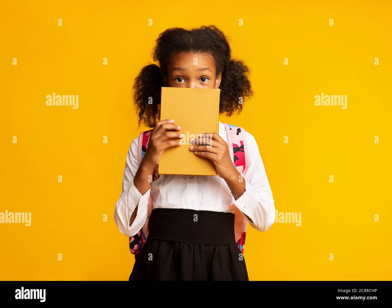 Shy African American Schulmädchen Versteckt Hinter Buch, Studio Shot Stockfoto