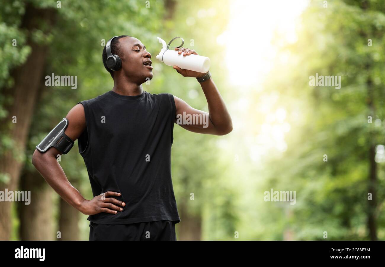 Durstiger schwarzer Sportler trinkt Wasser, joggt im Park Stockfoto