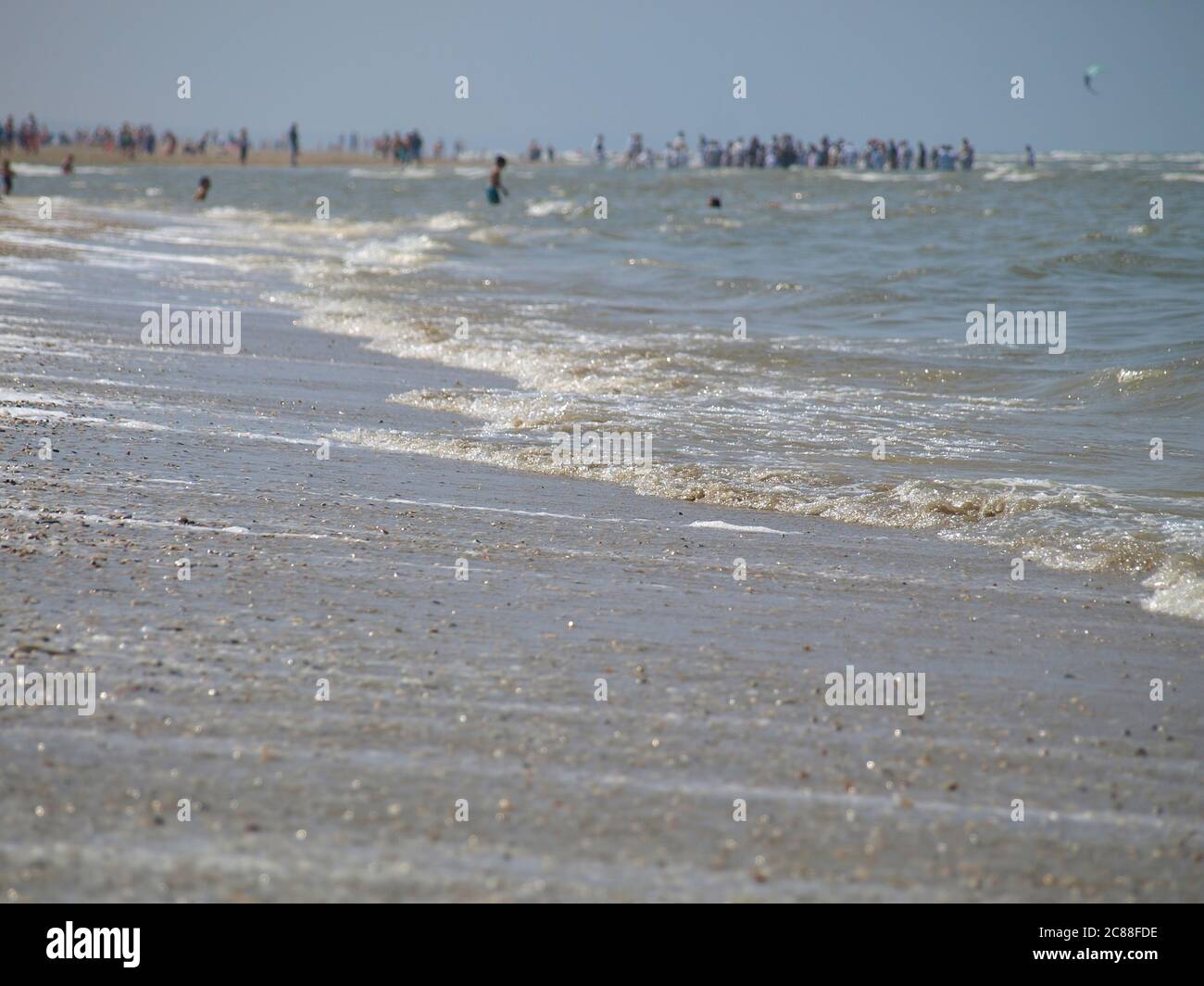 Ruhige Wellen am Strand der Nordsee in Katwijk/NL. Entfernte Menschen im unscharfen Hintergrund Stockfoto