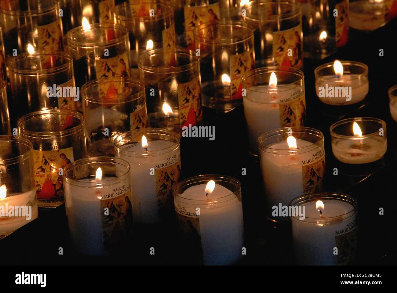 Leuchtende Votivkerzen erleuchten kleine Räume im dunklen Inneren der Basilika Sainte-Marie-Madeleine, der Kirche einer ehemaligen Benediktinerabtei in Vézelay, Yonne, Burgund, Frankreich. Die Kirche wurde im 12. Jahrhundert umgebaut und erweitert, um den Horden von Pilgern gerecht zu werden, die in der Krypta erhaltene Knochen verehren, die vermutlich Reliquien der Heiligen Maria Magdalena sind. Die Abteikirche wurde 1979 in die UNESCO-Liste des Weltkulturerbes aufgenommen. Stockfoto