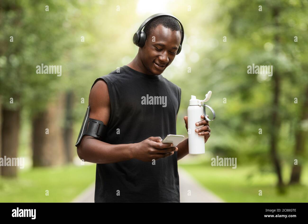 Glücklicher schwarzer Kerl mit Telefon und Trinkwasser, Training im Freien Stockfoto
