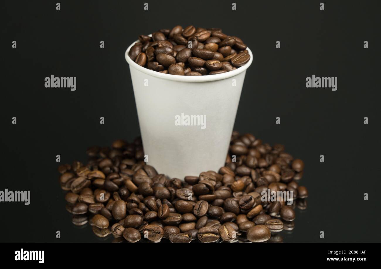 Papiertasse mit Kaffee und Kaffeebohnen auf dem Tisch Stockfoto