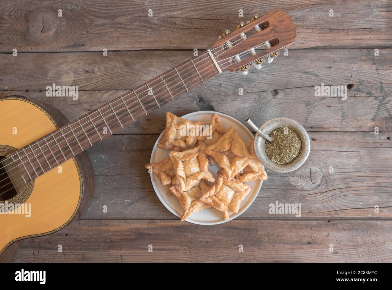 Overhead-Ansicht einer Gitarre, Mate und gebratenen Kuchen auf rustikalem Holzhintergrund Stockfoto
