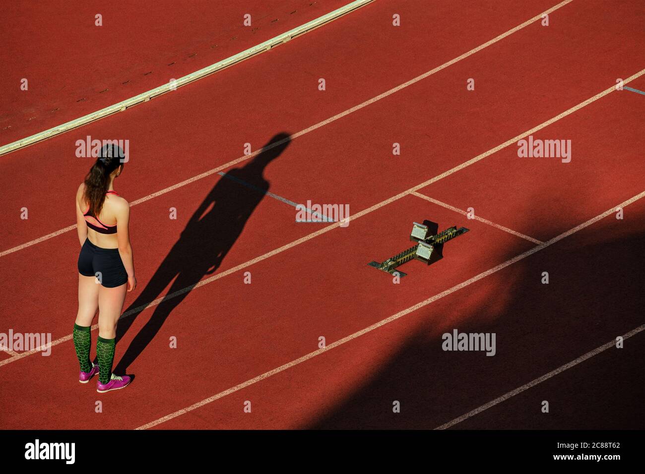 Mädchen Läufer stehen auf der Startlinie der roten Spur. Schatten ihres Körpers Stockfoto