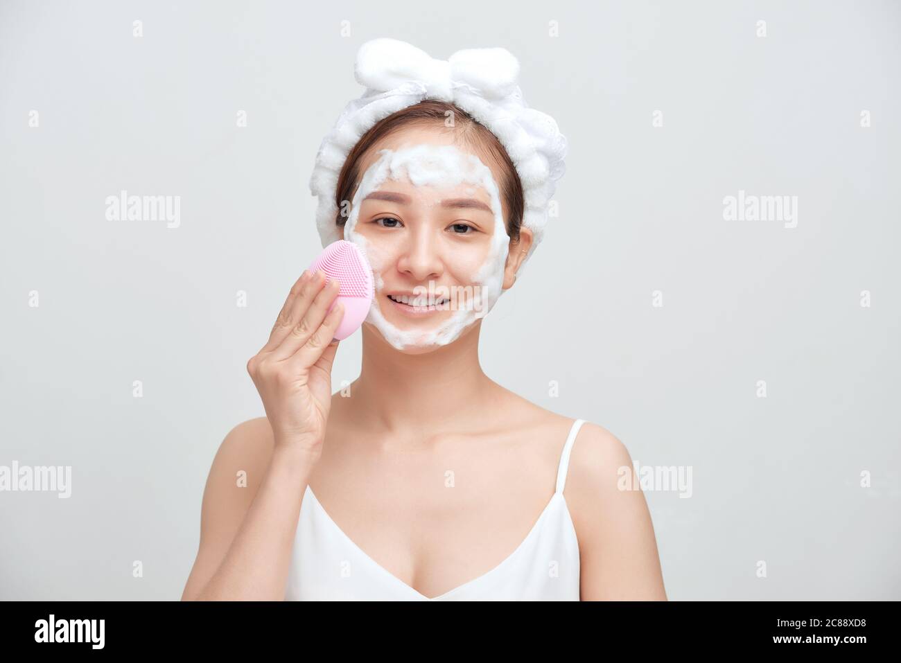 Glücklich junge asiatische Frau Anwendung schäumende Reinigungsmittel auf ihr Gesicht und tragen Handtuch auf ihren Kopf. Stockfoto