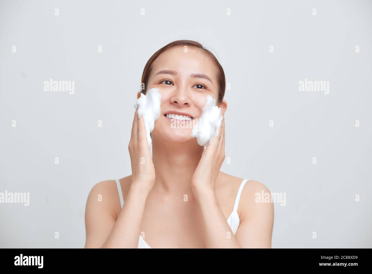 Glücklich attraktive junge asiatische Frau Anwendung schäumende Reinigungsmittel auf ihr Gesicht über weißem Hintergrund. Stockfoto