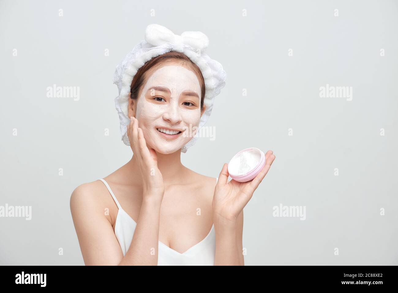 Glückliche junge asiatische Frau Anwendung Gesichtsmaske Ton und trägt ein Handtuch. Stockfoto