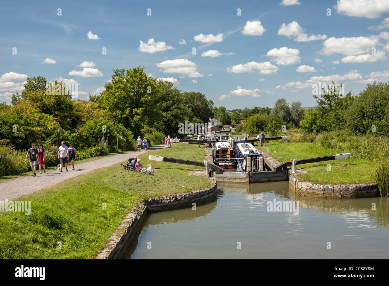 Zwei Schmalbooten nebeneinander an der Schleuse 31 von Caen Hill Locks, Devizes, Wiltshire, England, Großbritannien, während Familien den Schlepppfad hoch und runter laufen Stockfoto