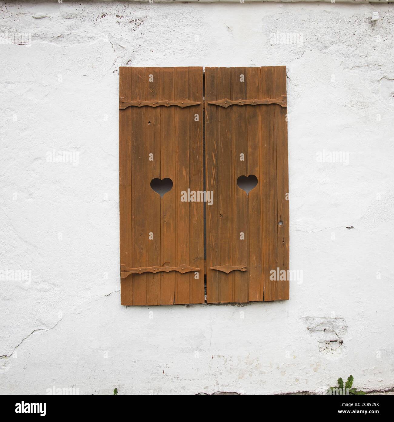 Geschnitzte hölzerne Fensterläden mit Herzen auf einer weißen Ziegelwand. Stockfoto