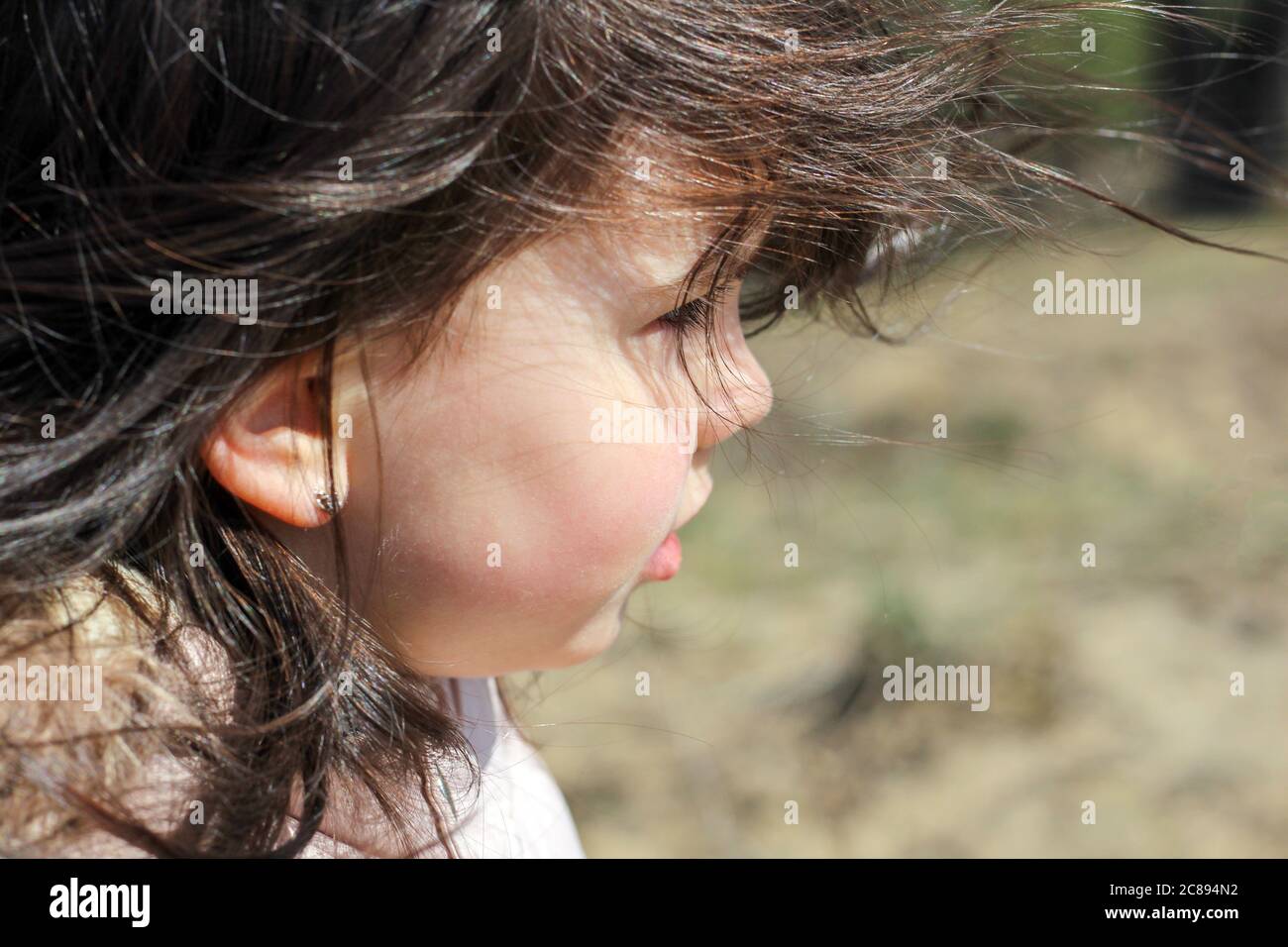 Profil und Nahaufnahme Porträt von wunderschönen kleinen Mädchen mit flatternden langen Haaren auf einem verschwommenen Hintergrund im Freien Stockfoto