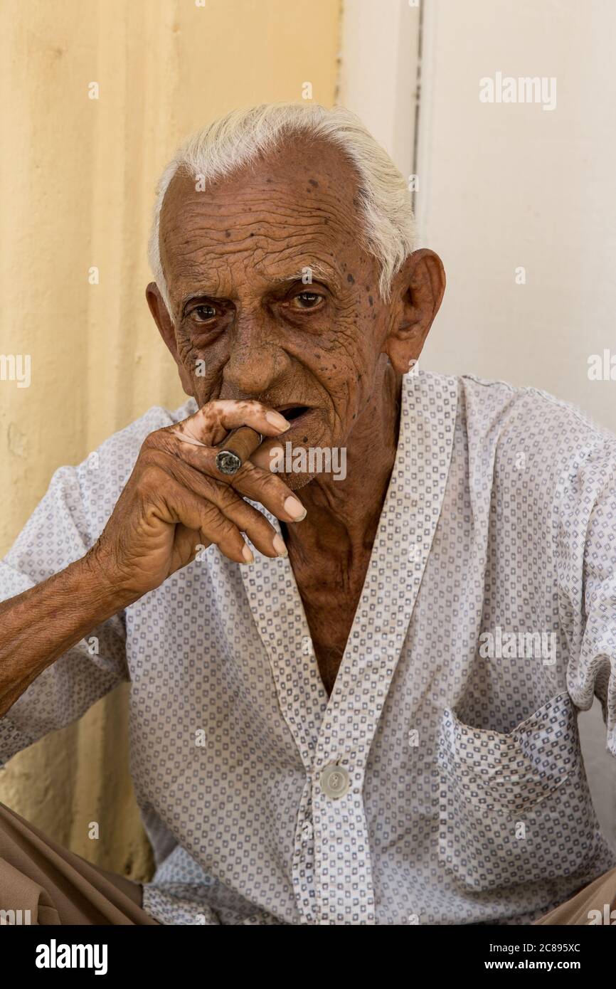 Havanna / Kuba - 04.15.2015: Nahaufnahme eines alten Kubaners, der auf der Straße sitzt und eine Zigarre raucht, in der Altstadt von Havanna, Kuba Stockfoto