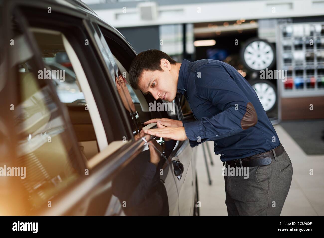 Der Car Service Manager fegt seine Hand über die Motorhaube eines Autos und überprüft das Gemälde im Sonnenlicht. Stockfoto