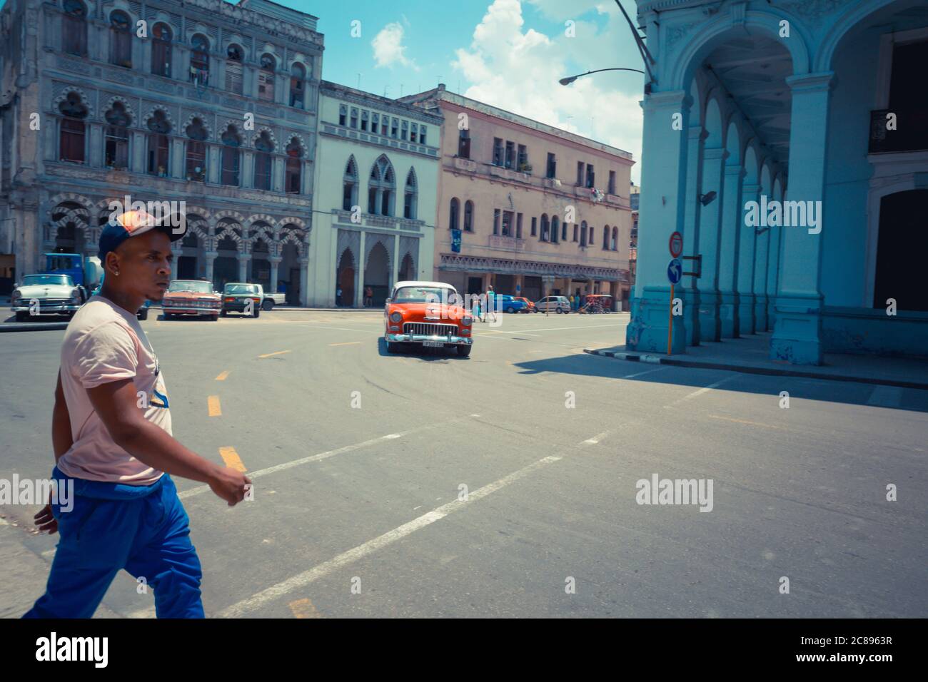 Havanna / Kuba - 04.15.2015: Kubaner mit Sportkleidung und Hut, der als roter Klassiker (Oldtimer) die Straße überquert, Havanna, Kuba Stockfoto