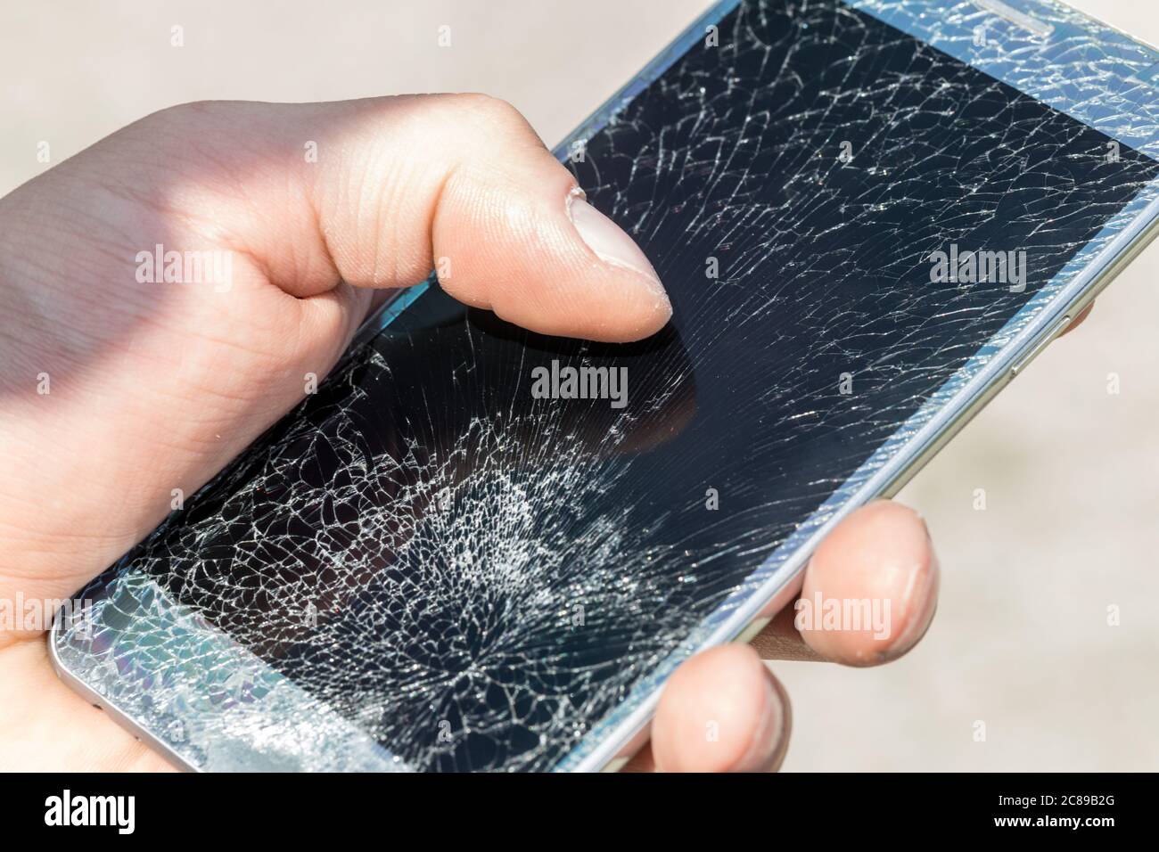 Ein junger Mann hält ein Telefon mit einem sehr geknackten Touchscreen Stockfoto